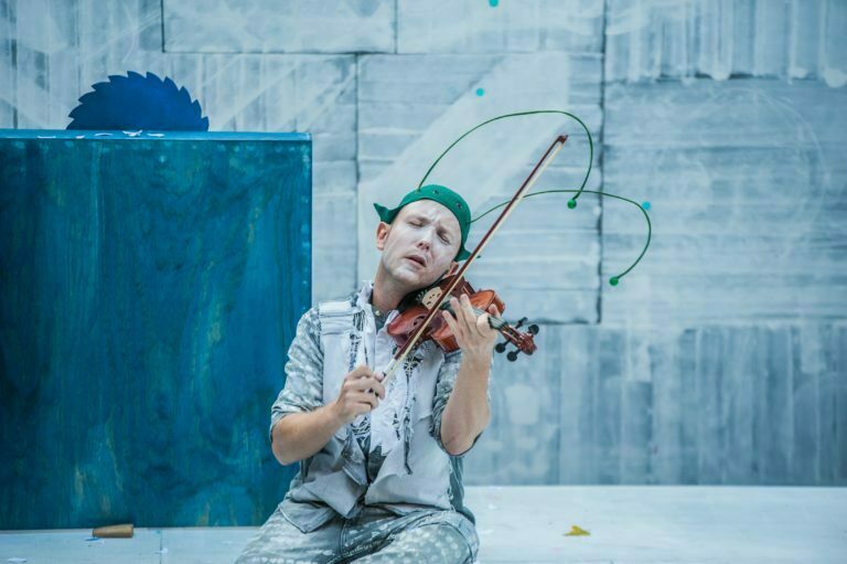 Zdjęcie ze spektaklu Pinokio. Aktor grający Świerszcza skupia się bardzo podczas gry na skrzypcach.