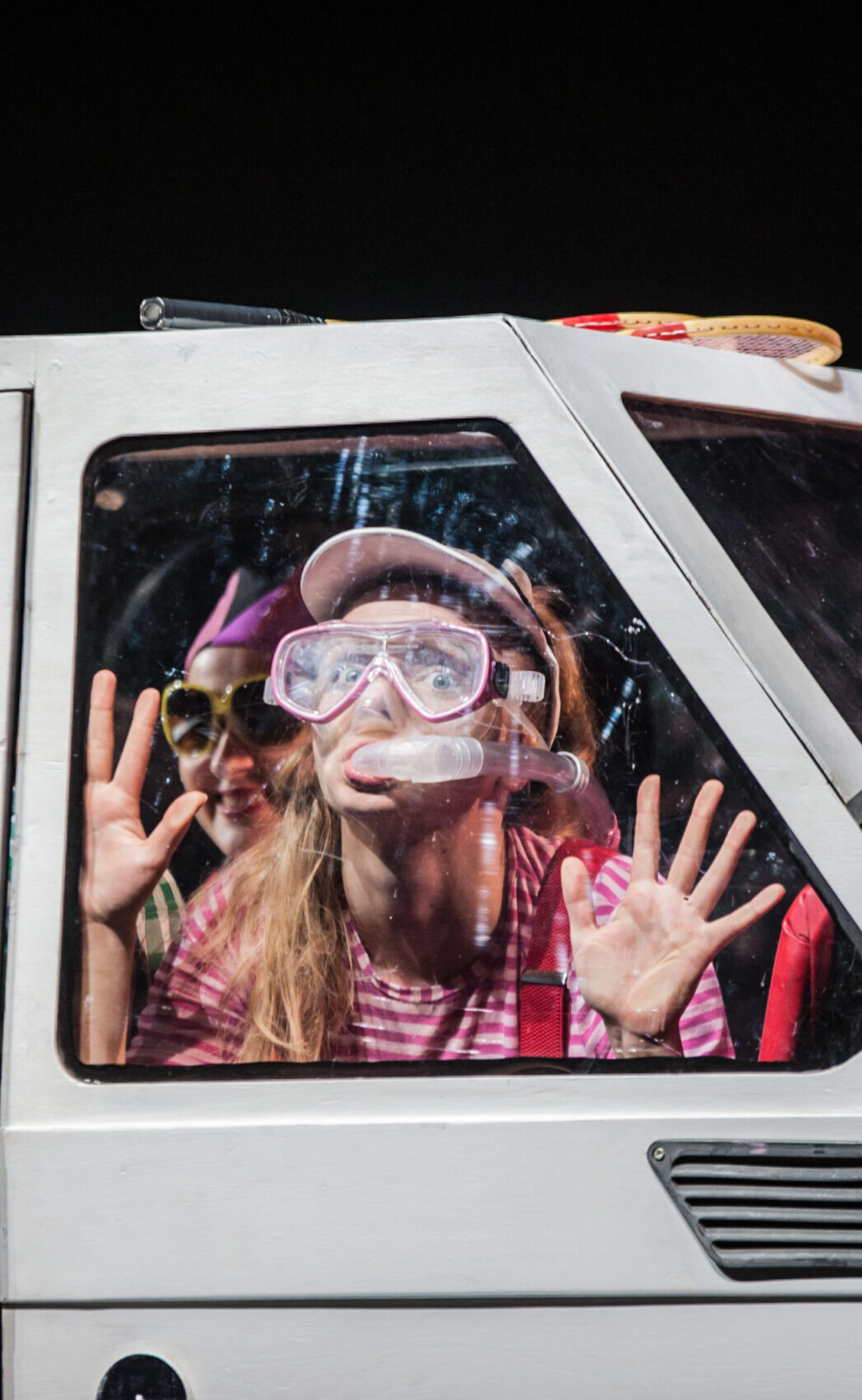 Zdjęcie ze spektaklu Ja, Maluch i morze. Mała dziewczynka siedząca w samochodzie ma na sobie okulary do nurkowania i maskę tlenową. Przyklejona jest do szyby.