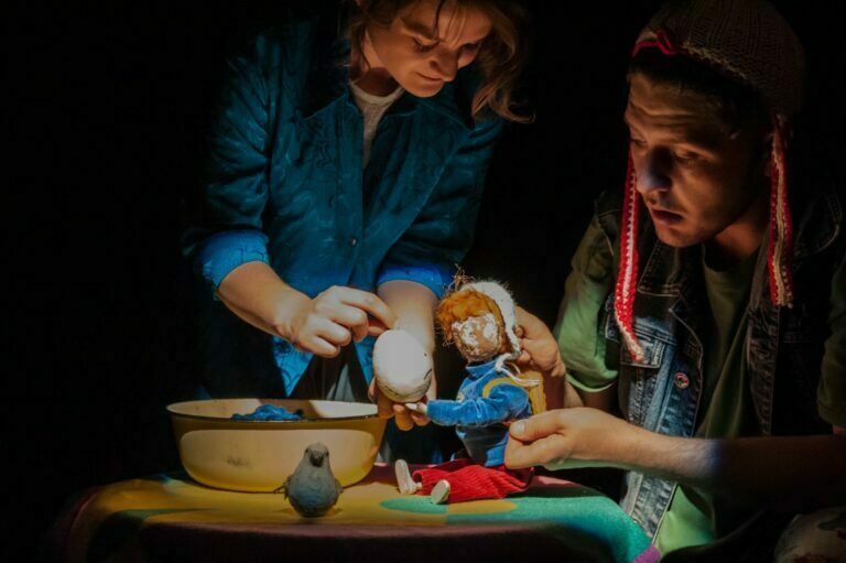 Scena ze spektaklu Teatru Baj pt. Nieopodalja. Młoda kobieta i młody męzczyzna animują postacią lalki przypominającą chłopca.