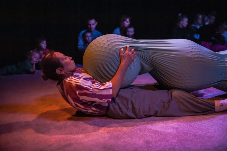 the actress is lying on her back and on top of her big two connected balls, the edge of one she holds with both hands. A performance for the youngest children from 0 to 3 years, showing the workings of internal organs. In this case, the intestines.