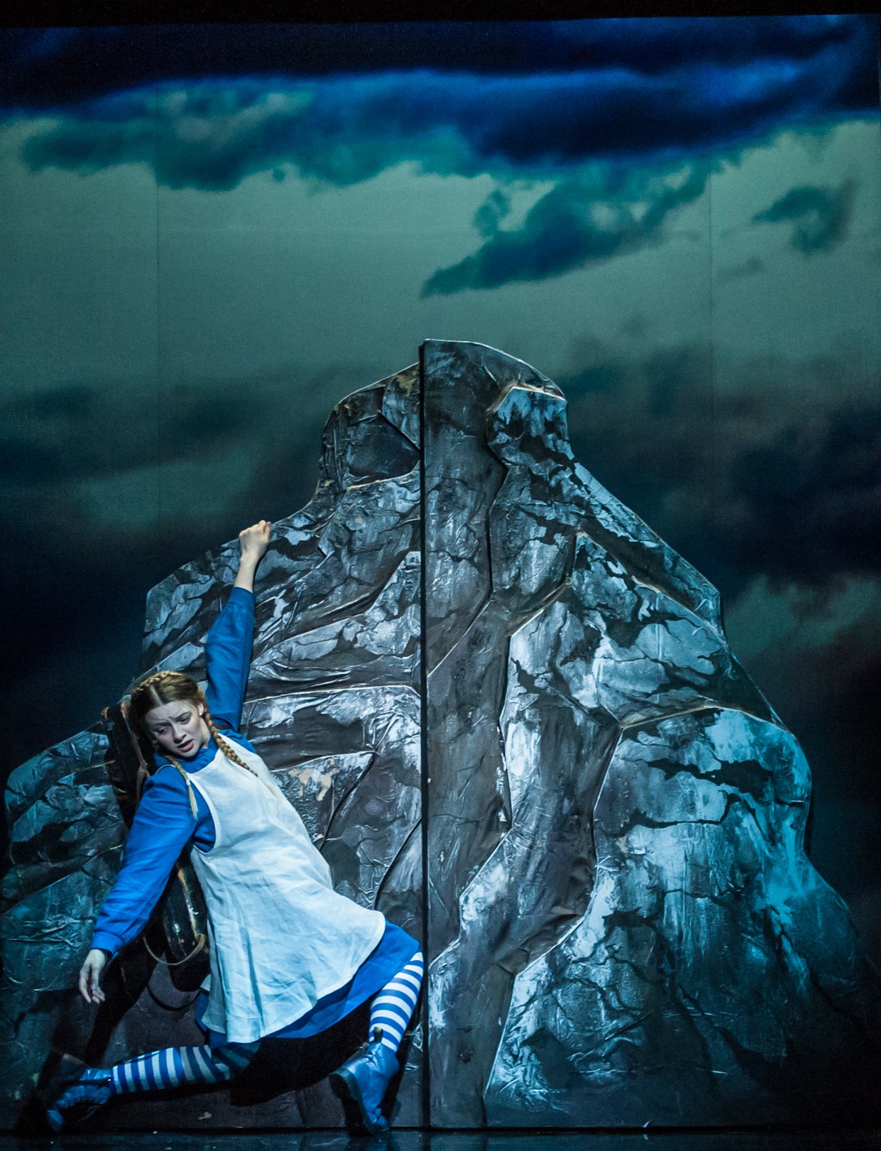A young girl climbs with difficulty up a large mountain rock. Above her stretches the night dark sky. Stills comes the play "The Fiddlee Girl"