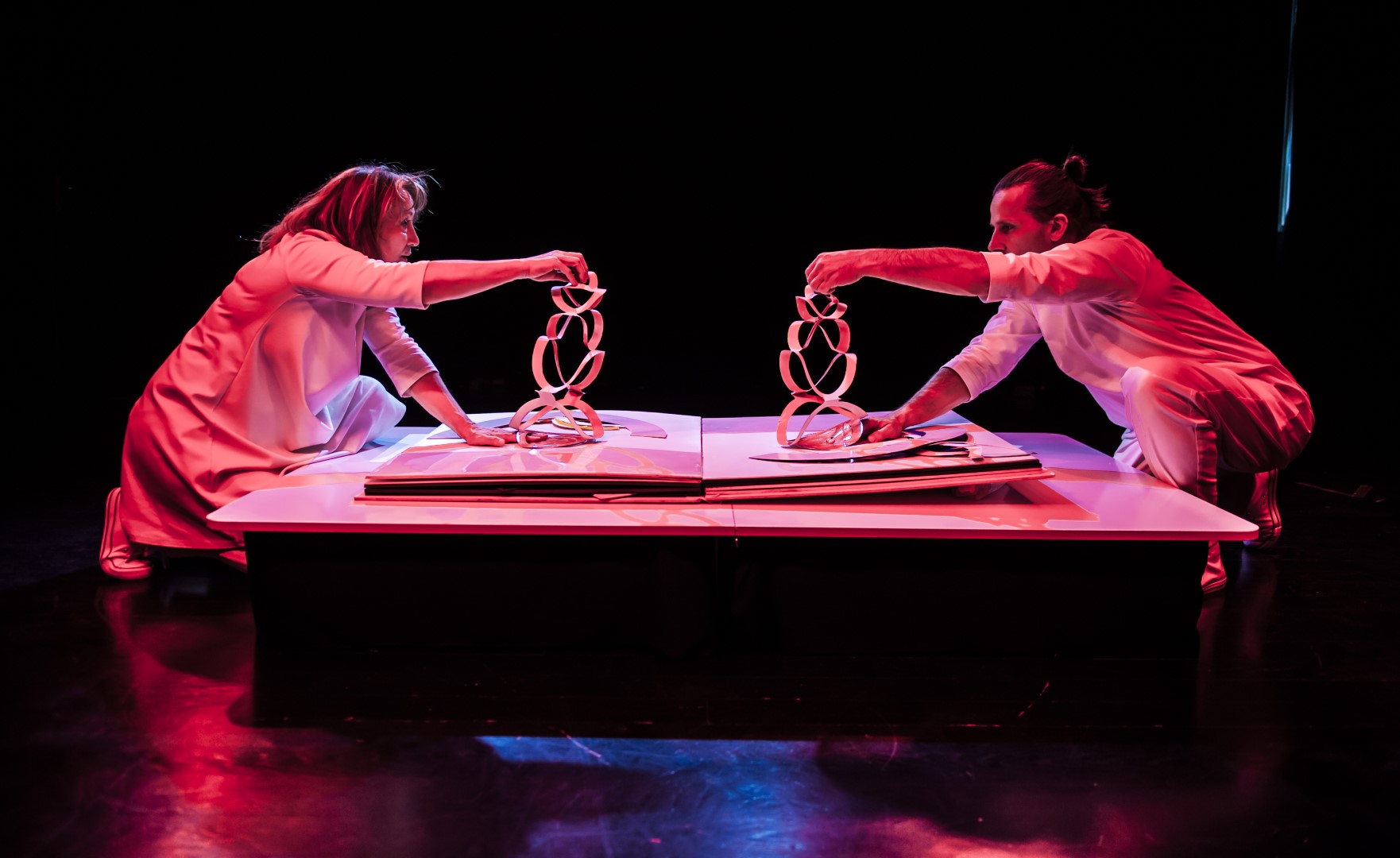 Scena ze spektaklu pt. "Ksiiazeczka" przedstawia dwoje aktorów ubranych na biało posługujący się formami origami które leżą na wielkiej książce